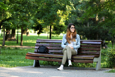 Portrait of young woman sitting on bench in park