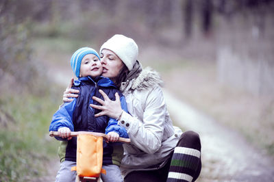 Mother kissing son riding bicycle at park during winter