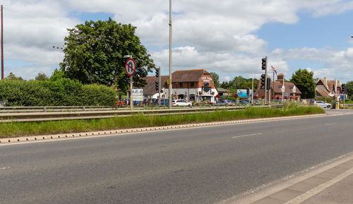 Road by trees and buildings against sky