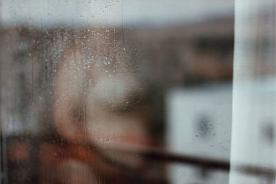 Defocused image of naked woman standing behind wet window