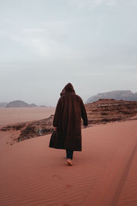 Rear view of woman standing on sand at desert against sky