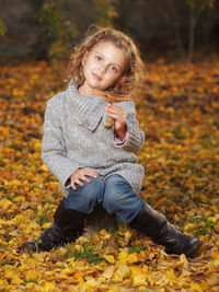 Portrait of smiling cute girl sitting on field during sunset