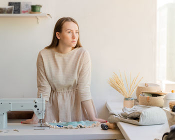 Thoughtful young woman fashion designer or atelier owner looking at window and thinking