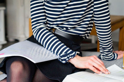 Midsection of woman with books sitting on sofa at home