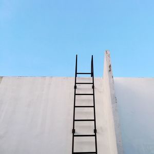 Low angle view of ladder on concrete wall against clear blue sky