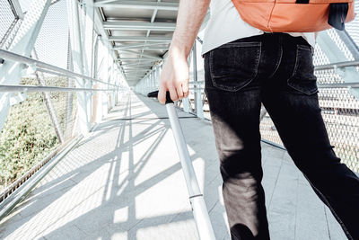 Midsection of man carrying suitcase on footbridge