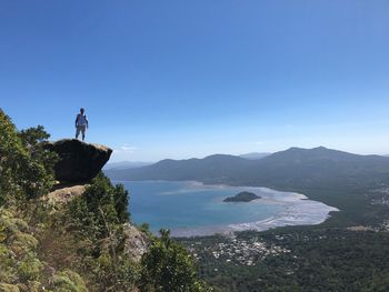 Man standing on rock by sea against blue sky