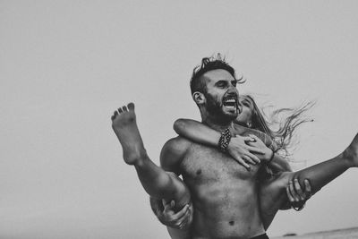 Shirtless man and woman standing against sky