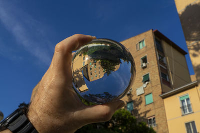 Low angle view of hand holding glass building against sky