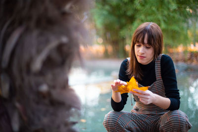 Woman holding maple leaf against lake