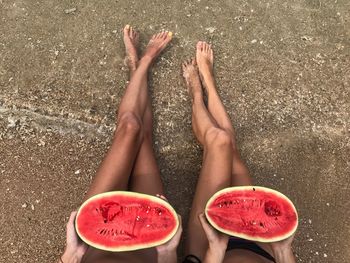 Low section of female friends eating watermelon on shore at beach