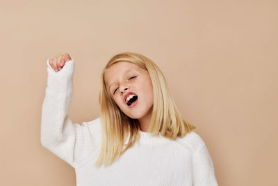 Cute girl with hand raised against beige background