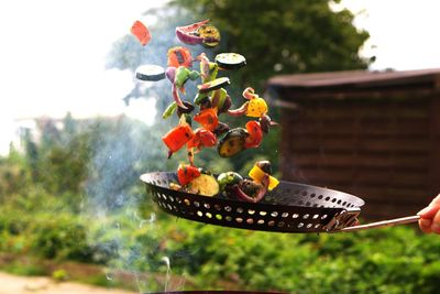 Cropped hand tossing vegetables while cooking outdoors