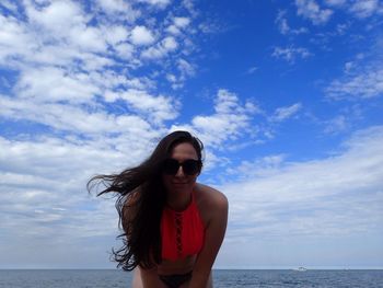 Portrait of young woman in sunglasses standing at beach against sky