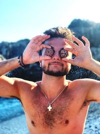 Shirtless young man holding seashells while standing at beach