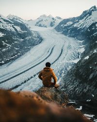 Rear view of man sitting on snowcapped mountain