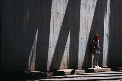 Woman standing on footpath against wall