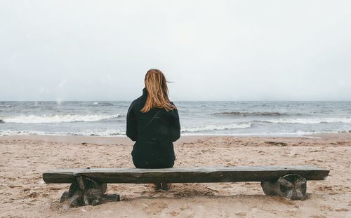 Rear view of woman standing on beach against clear sky