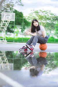 Full length of young woman sitting at basketball court