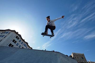 From below of young brave male skater jumping with skateboard and performing stunt in skate park on sunny day against blue sky