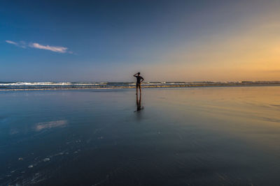 Silhouette man standing on beach against sky during sunset