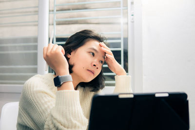 Portrait of young woman using mobile phone while sitting on table