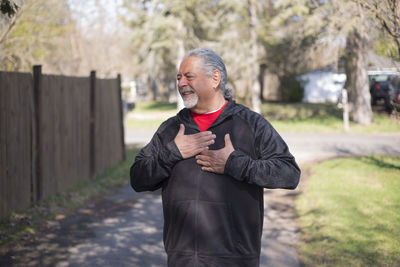 Smiling senior man gesturing while standing on footpath at park