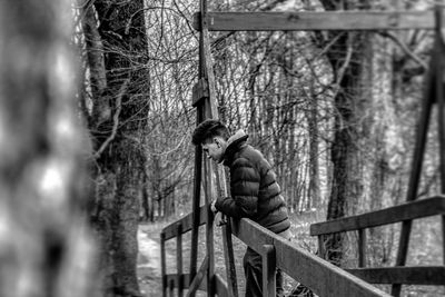 Side view of young man standing by railing in forest