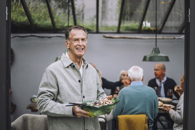 Portrait of smiling senior man holding salad bowl at dinner party