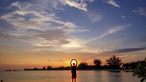 Man standing by lake against sky during sunset