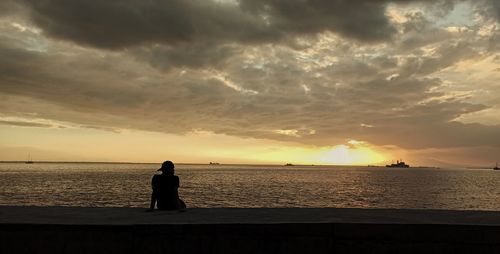 Silhouette man looking at sea against sky during sunset