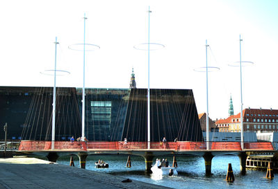Sailboats in river by buildings against clear sky