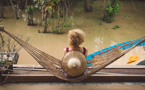 High angle view of woman sitting on hammock by swamp in forest