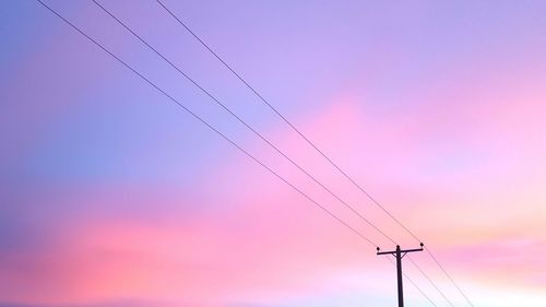 Low angle view of electricity pylon against sky at sunset