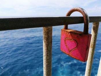 Close-up of heart shape on padlock locked with railing against sea