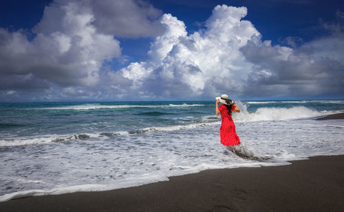 Rear view of woman standing on beach against sky