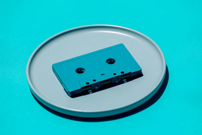High angle of old fashioned compact cassette placed on round shaped plate on blue background in studio