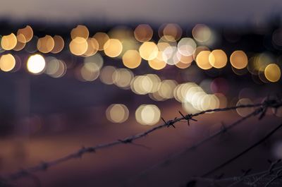 Close-up of barbed wire against illuminated lights at night