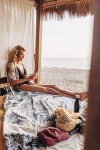 Woman reading book while sitting in hut on vacation at beach
