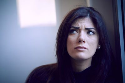 Close-up of worried woman looking away by window