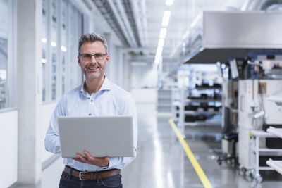 Manager on shop floor of factory using laptop