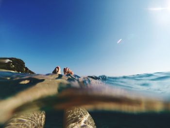 Low section of woman swimming in sea against clear blue sky on sunny day