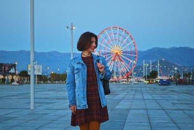 Woman standing by ferris wheel against clear sky