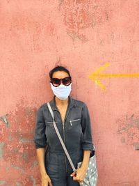 Portrait of woman wearing mask standing against wall