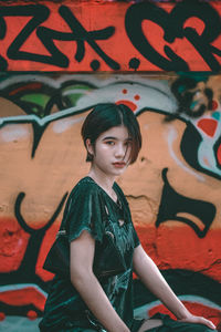 Full length of young woman standing against graffiti wall