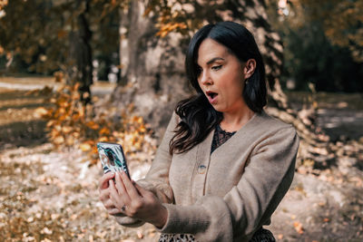 Young woman using mobile phone, autumn, fall, excited, shocked.