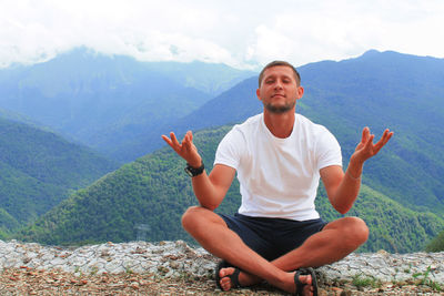 Man sitting and meditating against mountains
