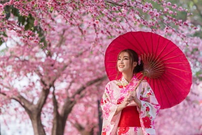 Low angle view of woman holding pink cherry blossom