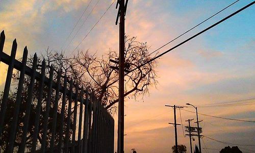 Low angle view of electricity pylon against cloudy sky