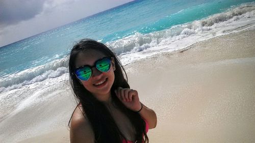 Portrait of smiling young woman at beach against sky